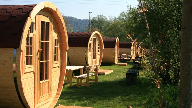 Wooden cabins with arched windows and doors, outdoor seating, and a grassy area. - NATURAMA Beilngries (Beilngries)
