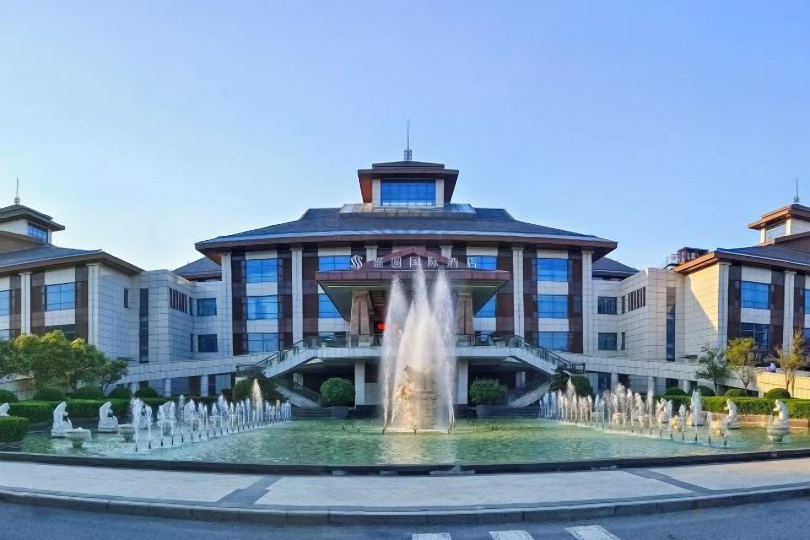 A hotel with a central fountain, a covered entrance, and a symmetrical facade.