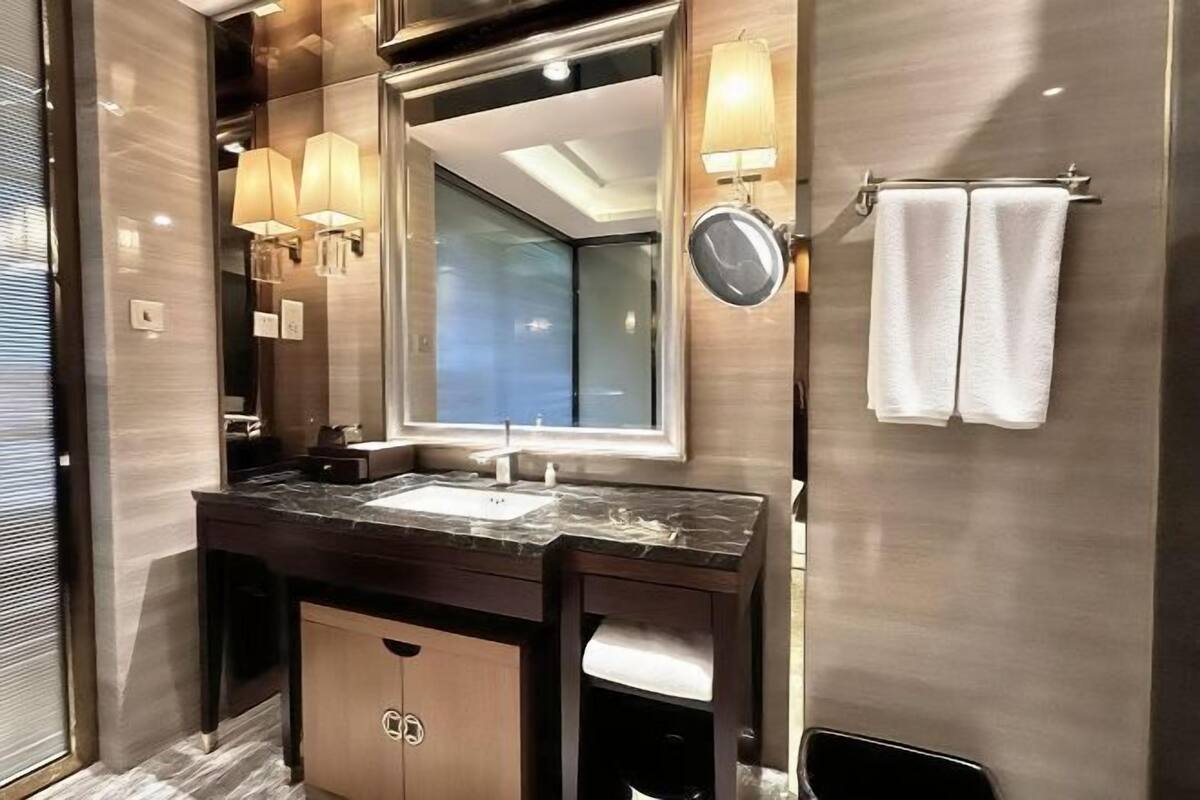 Une salle de bain moderne avec un lavabo en marbre, un grand miroir, des appliques murales et un porte-serviettes.