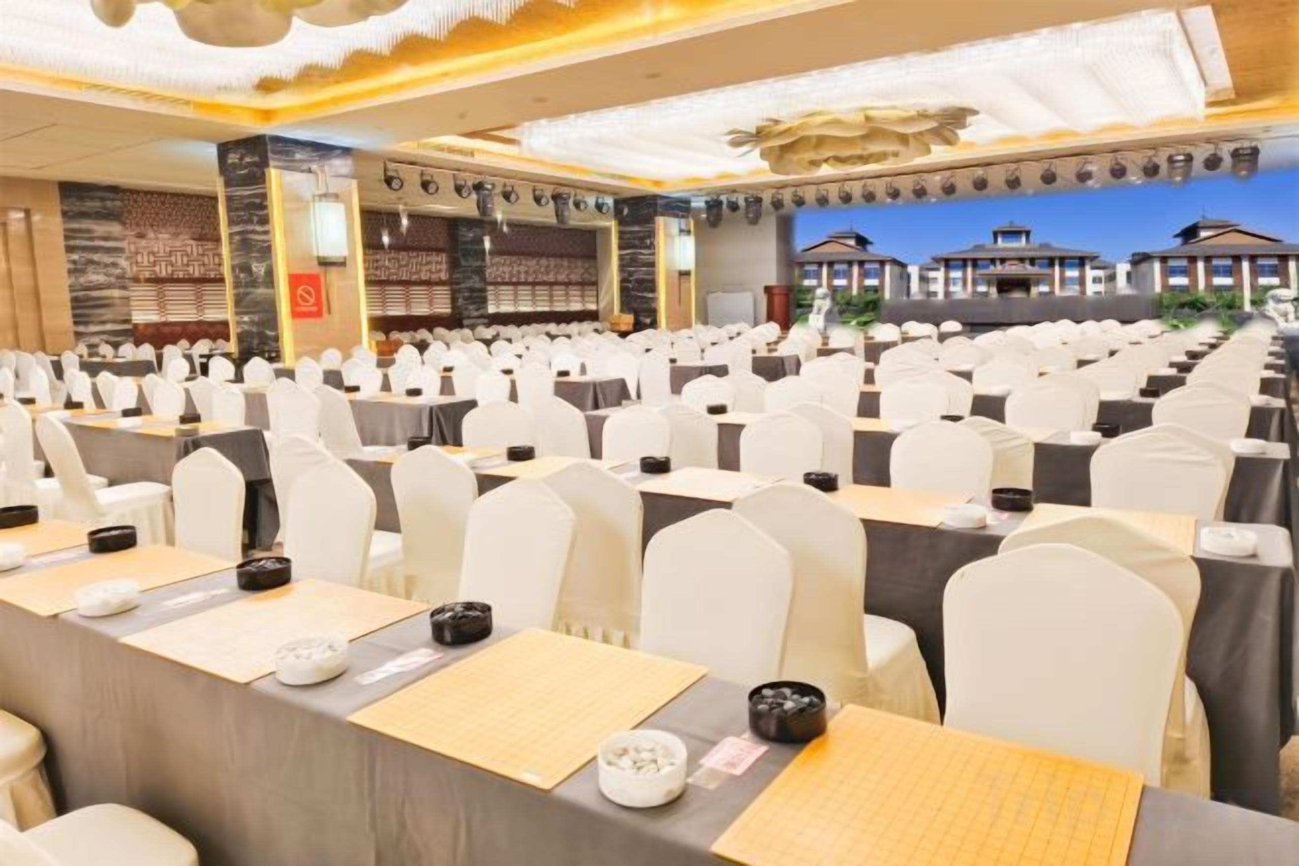 Un salón de banquetes con filas de mesas, sillas blancas y un escenario.