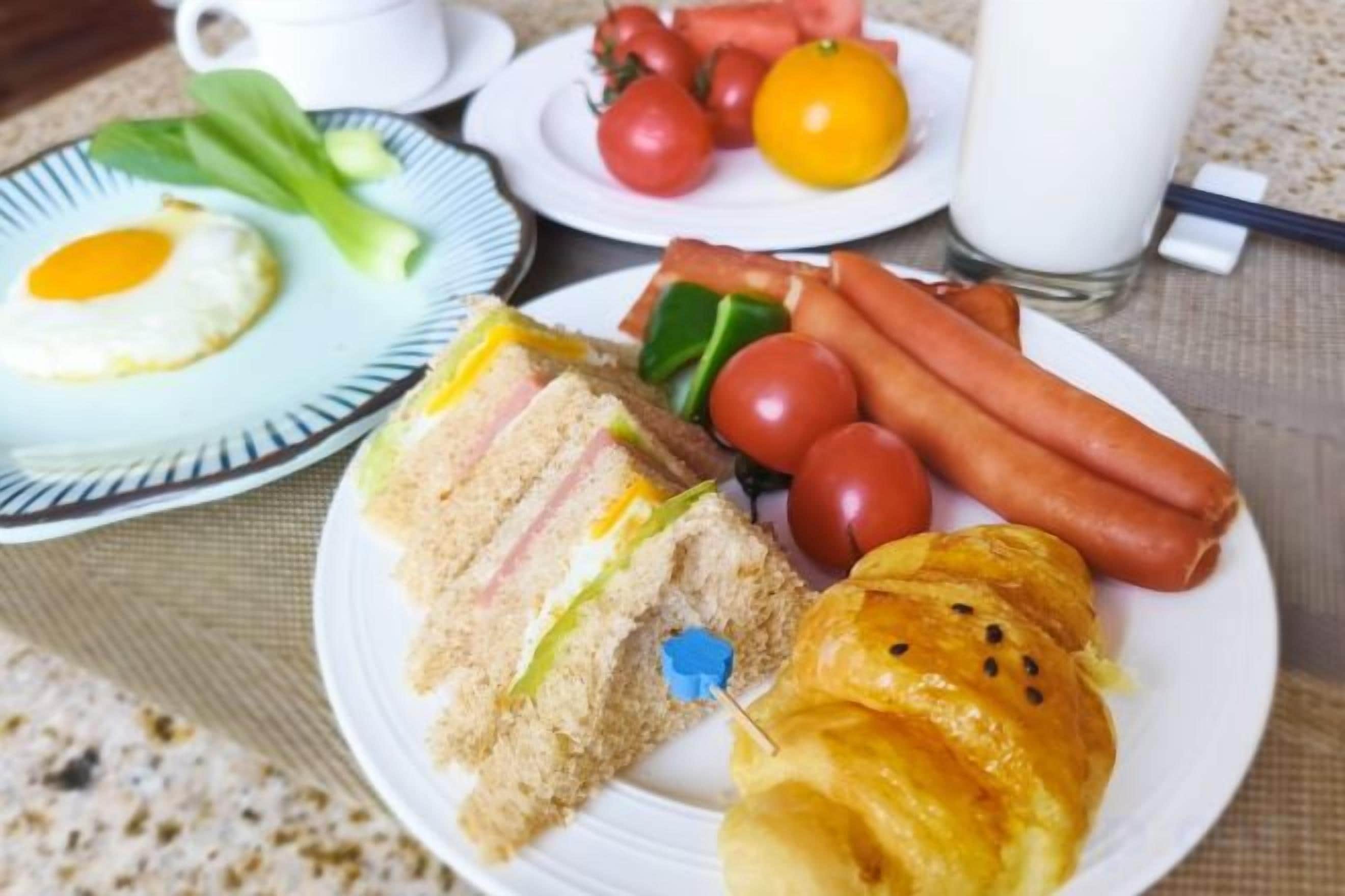 Ein Frühstücksteller mit Eiern, Schinken, Käse, Gemüse, einem Croissant sowie einer Anordnung aus Tomaten und Orangen.