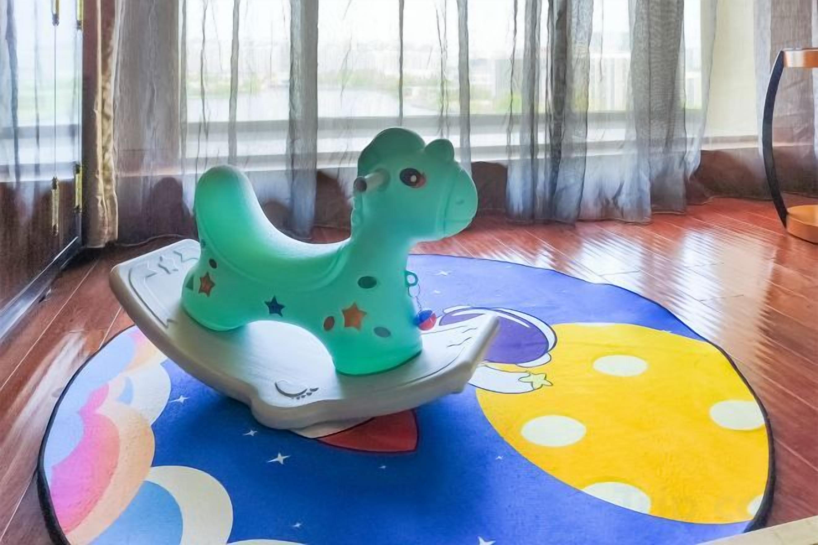 A green rocking horse on a colorful mat with a moon and stars design.