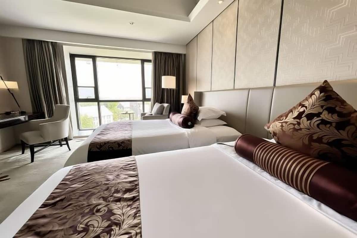 Une chambre d’hôtel avec deux lits, un bureau, une chaise et une grande fenêtre.