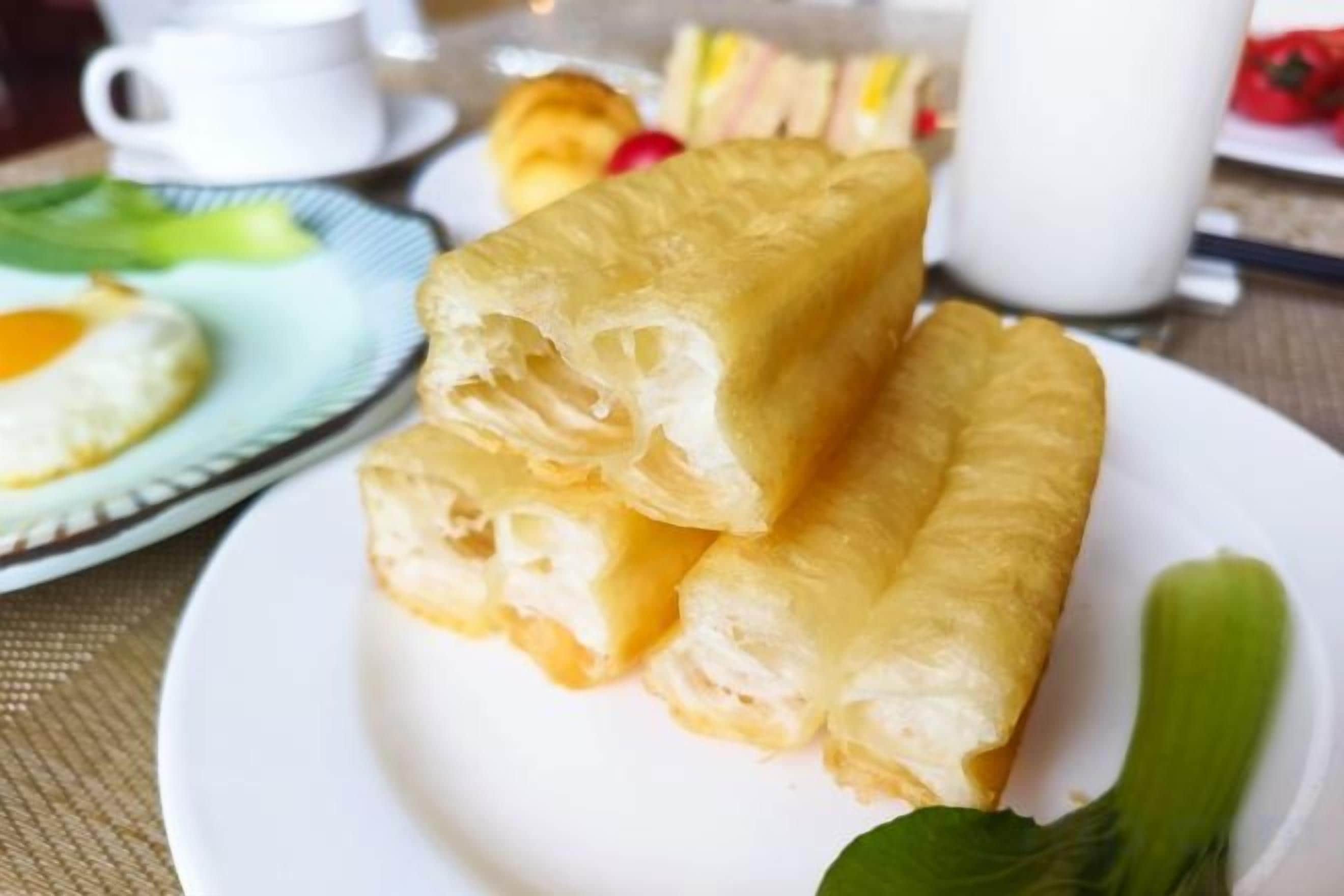 A plate with a food item, possibly a pastry, on a table with a cup and a plate with a green leaf.