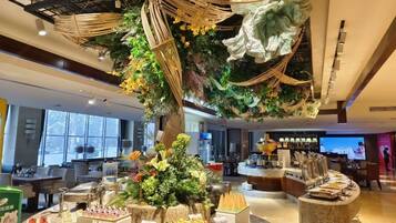 A hotel lobby with a central decorative tree, seating areas, and a reception desk.
