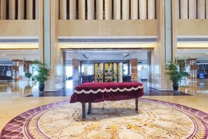 Un hall d’entrée avec un grand tapis rond au centre, une table rouge bordée de blanc et, au fond, un comptoir d’accueil.