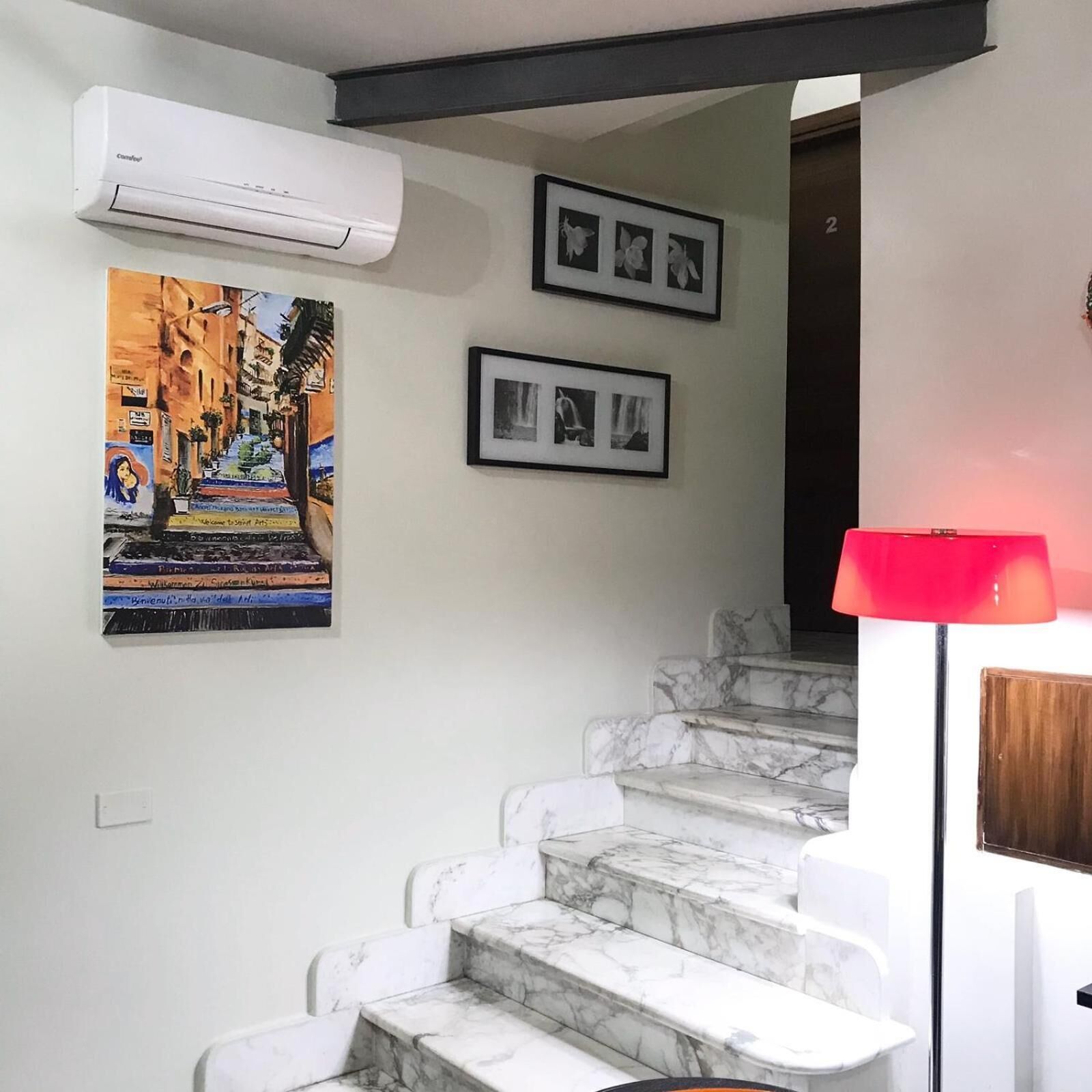 Una escalera con escalones de mármol que lleva a una plataforma, una unidad de aire acondicionado montada en la pared y dos fotografías enmarcadas sobre la escalera.