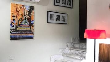 Una escalera con escalones de mármol que lleva a una plataforma, una unidad de aire acondicionado montada en la pared y dos fotografías enmarcadas sobre la escalera.