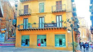 Un edificio amarillo con un letrero que dice 'Bed & Breakfast D'Arte', con un balcón lleno de plantas y una vitrina con ropa.