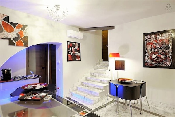 A modern hotel lobby with a glass table, a staircase, and artwork on the walls.