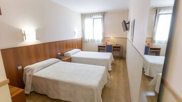 Une chambre d’hôtel avec deux lits, une tête de lit en bois, un bureau avec une chaise, une petite table et un miroir.