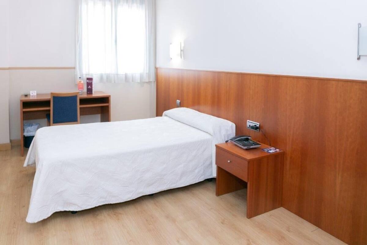 Et hotelværelse med en enkelt seng, et trænatbord, et skrivebord og en stol.