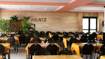 Ein Restaurant mit mehreren Tischen und Stühlen, einer Holzwand mit dem Schriftzug 'ARATZ' und einer Tür mit der Aufschrift 'SALIDA'.