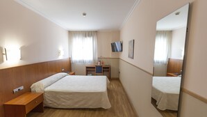 A hotel room with two beds, a desk, a TV, and a mirror. - Andamur San Roman (San Millan)