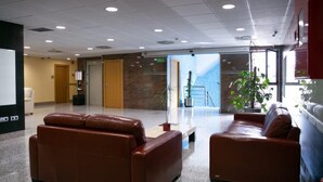 A lobby with two leather sofas, a reception desk, a staircase, and a view of a mountain through a glass wall. - Andamur San Roman (San Millan)