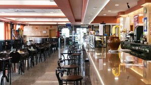 A restaurant with multiple tables and chairs, a bar area with a coffee machine, and a large decorative vase. - Andamur San Roman (San Millan)