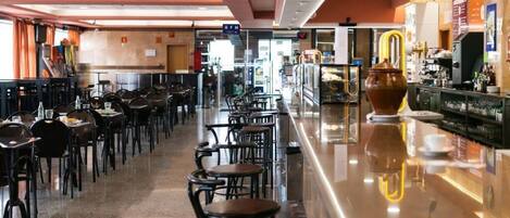 Un restaurante con varias mesas y sillas, una zona de bar con una máquina de café y un gran jarrón decorativo.