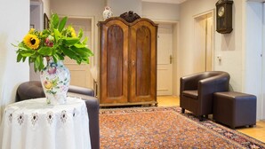 A room with a large wooden wardrobe, a floral vase with sunflowers, a patterned rug, and two leather armchairs. - Hotel Brunnenhof (Hanau)