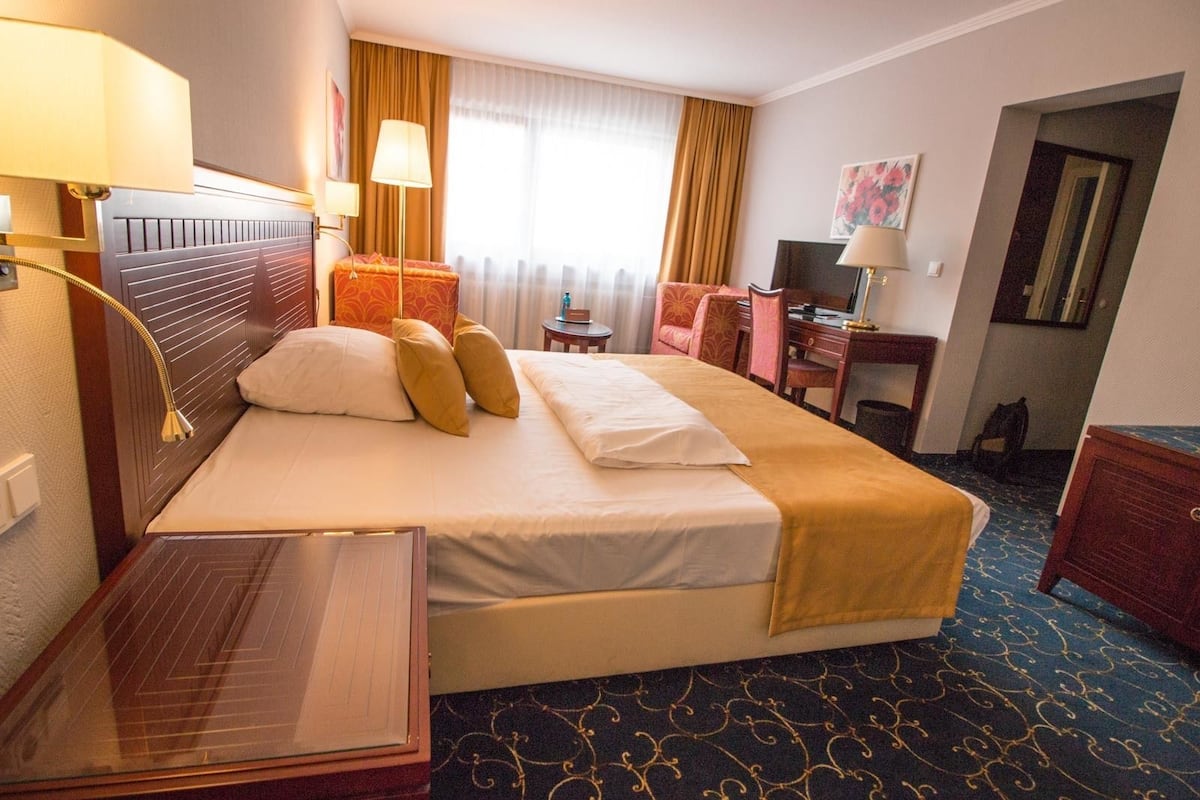 A hotel room with a large bed, bedside tables, a desk, a chair, and a television.