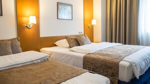 A hotel room with two beds, each with a patterned bedspread, a framed picture on the wall, and two wall-mounted lamps. - Hotel Brunnenhof (Hanau)