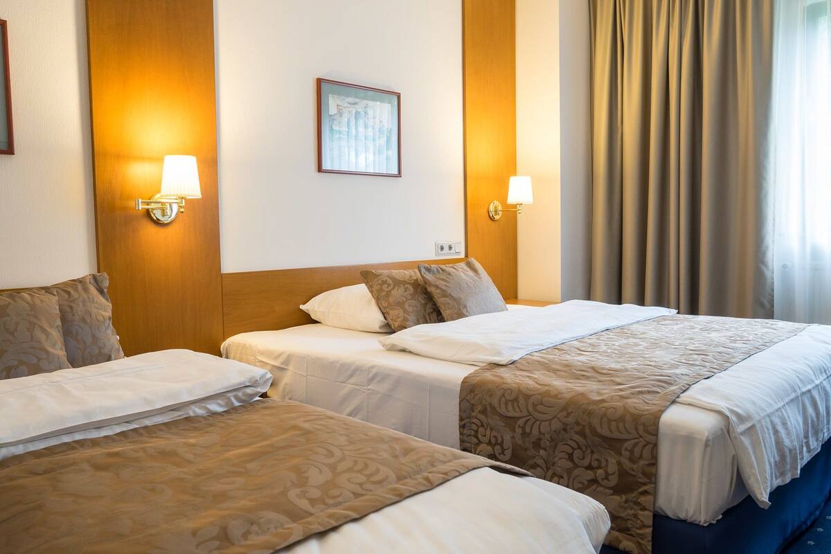 A hotel room with two beds, each with a patterned bedspread, a framed picture on the wall, and two wall-mounted lamps.