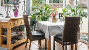 A conservatory with a table and chairs, surrounded by potted plants and a wooden desk with a lamp. - Hotel Brunnenhof (Hanau)