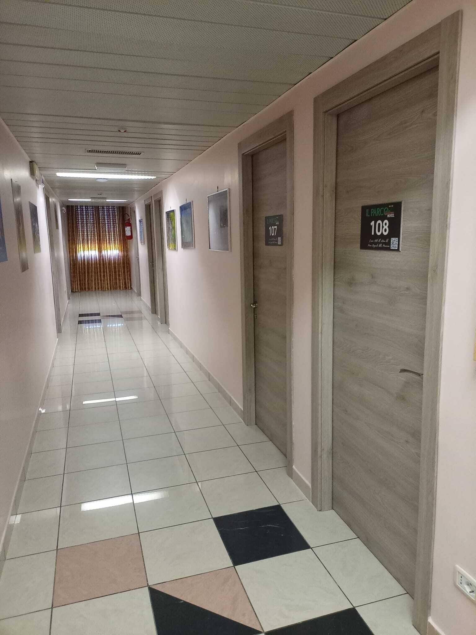 Un pasillo de hotel con suelo de baldosas, puertas con los números 107 y 108, y un extintor en la pared.