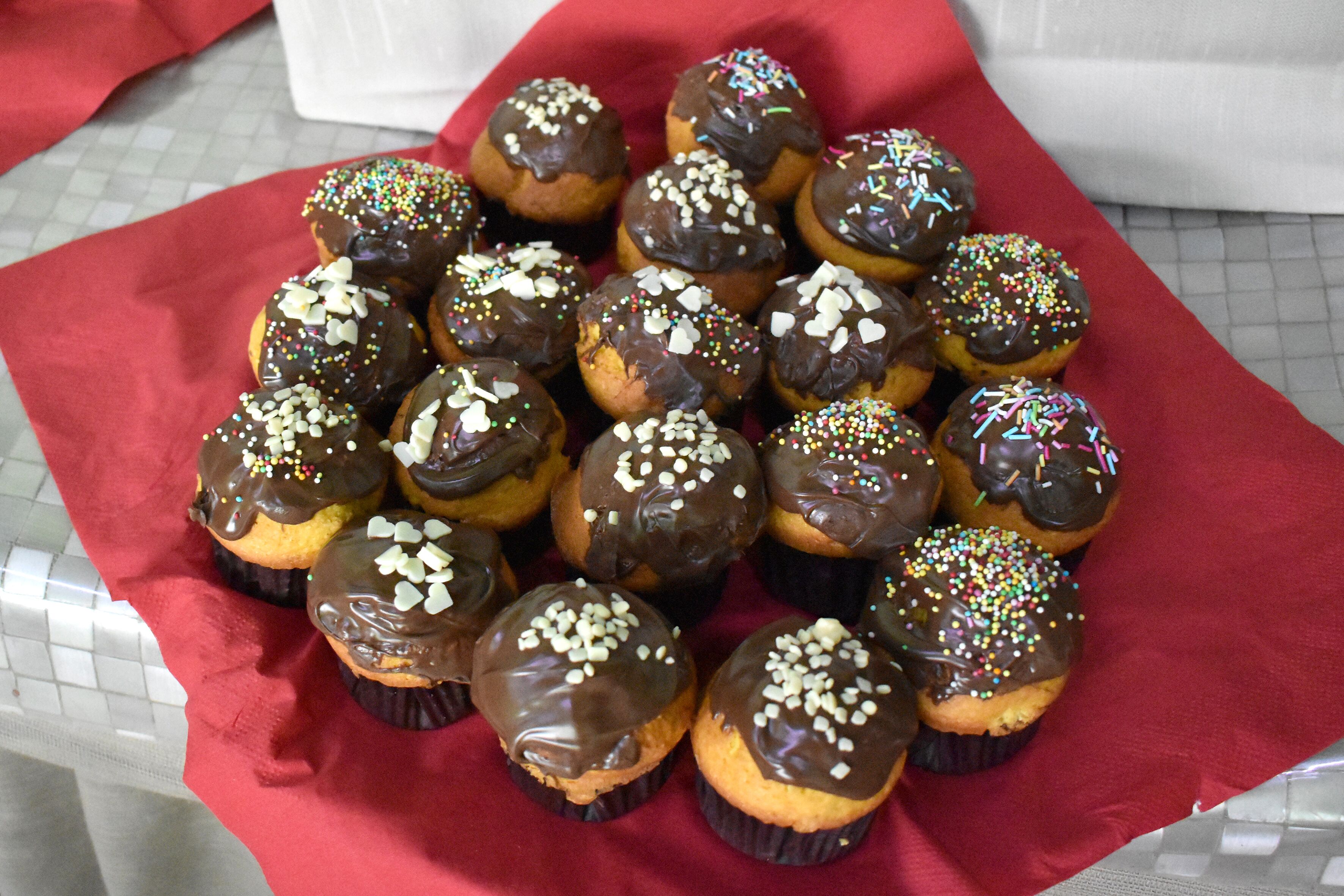 A tray of chocolate-covered cupcakes with sprinkles on a red cloth.