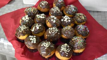 A tray of chocolate-covered cupcakes with sprinkles on a red cloth.