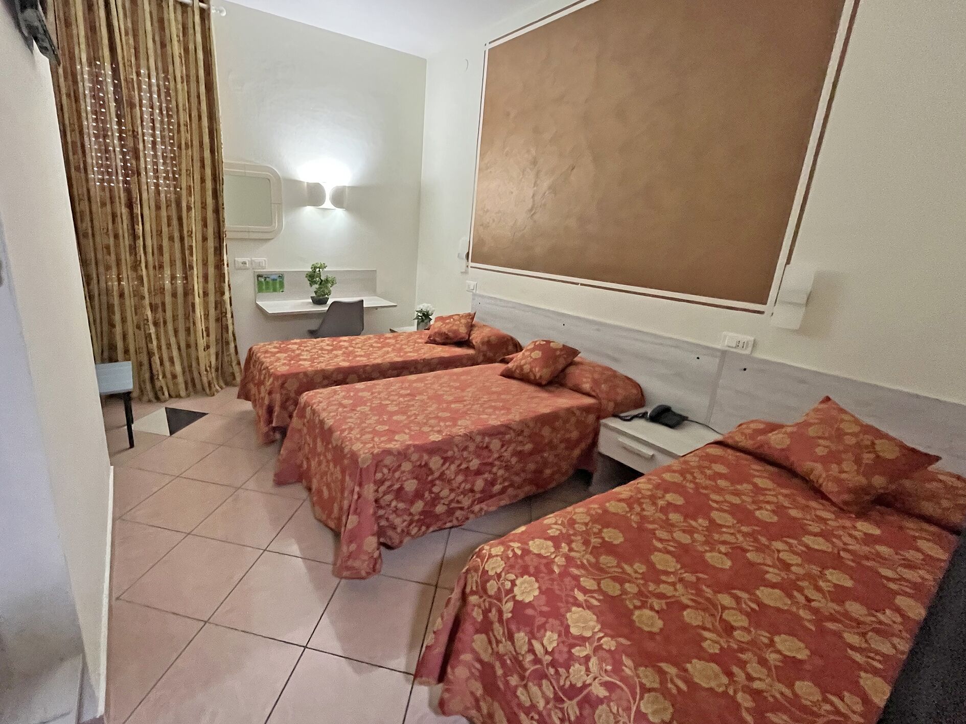 Habitación de hotel con dos camas individuales, un escritorio, una silla, una mesita, una planta en maceta y un ventanal grande.