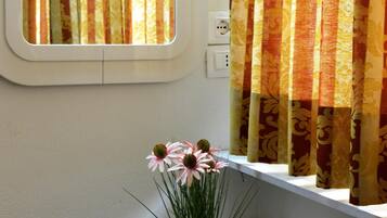 Ein Fenster mit Vorhängen, einer Steckdose und einer Vase mit Blumen auf einem Fensterbrett.
