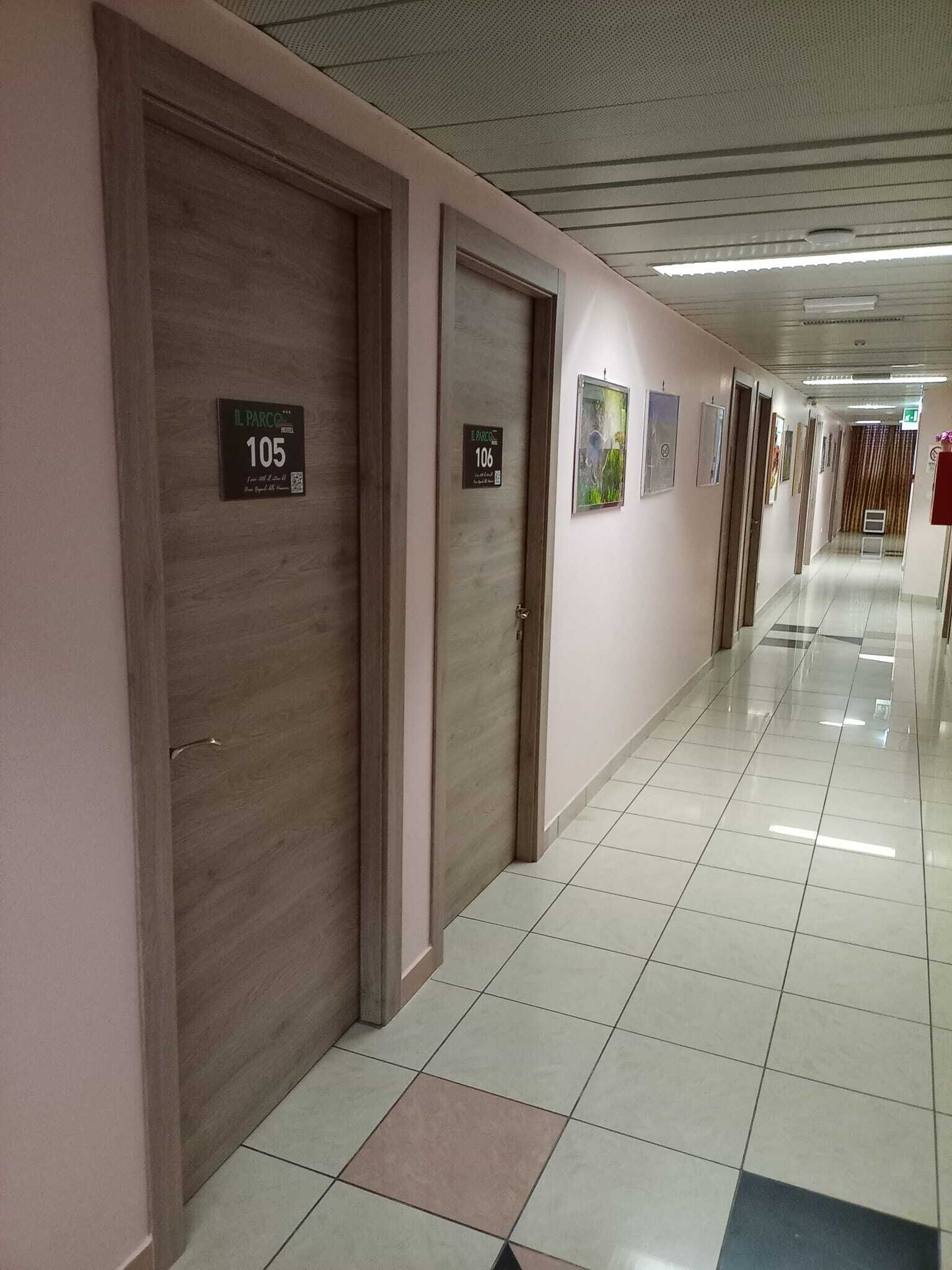 A hotel corridor with doors labeled 105 and 106, a tiled floor, and framed pictures on the walls.