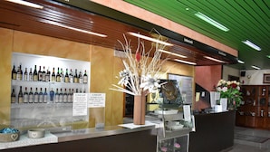 Un mostrador de recepción con una exhibición de botellas de vino, un jarrón con ramas decorativas y un techo verde.