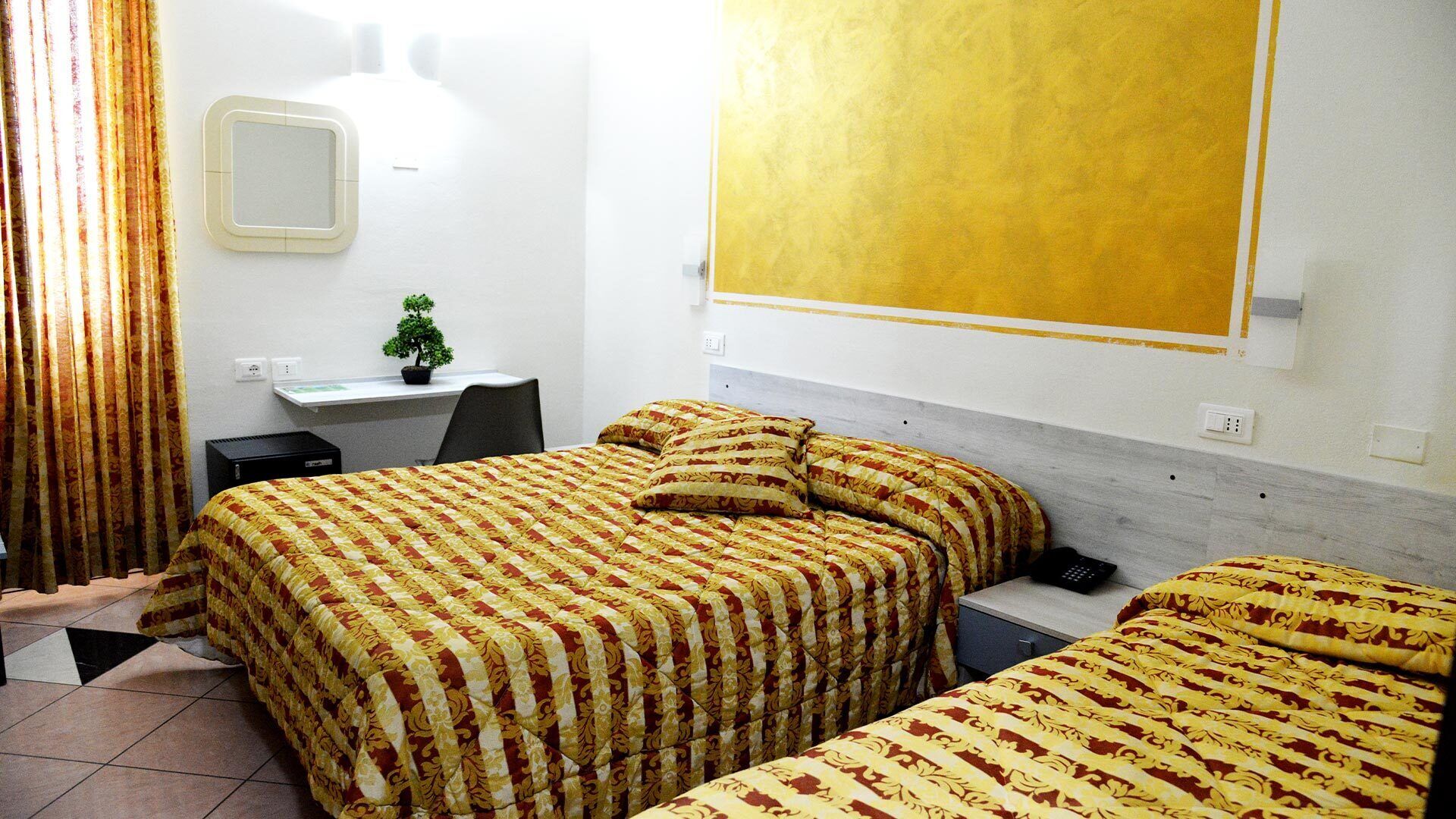 Une chambre d’hôtel avec deux lits, un bureau, une chaise, une petite plante en pot et une grande fenêtre.