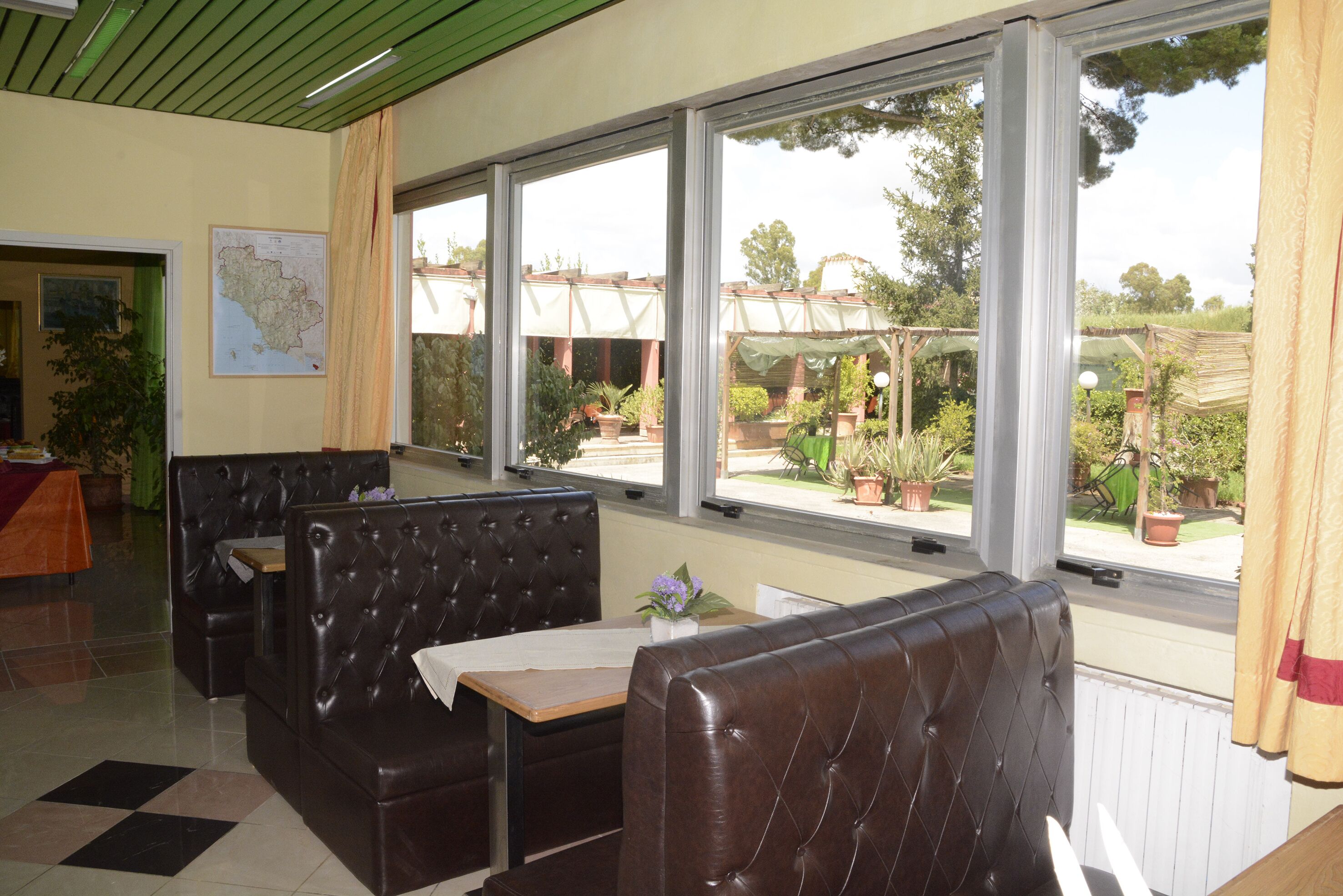 A restaurant with leather booths and a view of the garden through large windows.