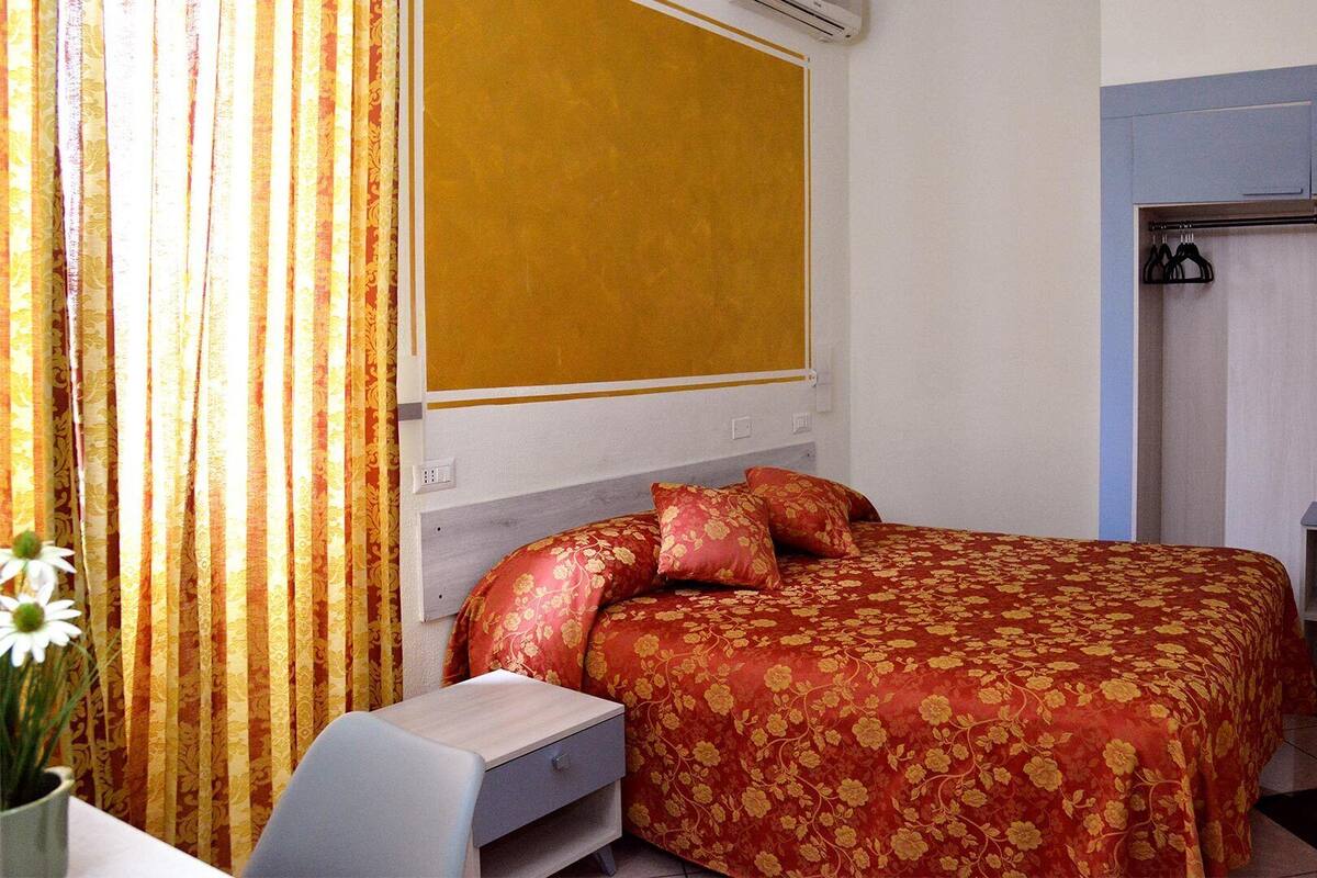 Une chambre à coucher comprenant un lit, une table de chevet, une armoire et une fenêtre avec des rideaux.