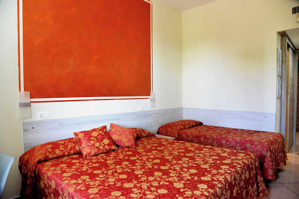 Une chambre d’hôtel avec deux lits, chacun agrémenté d’une literie à motifs floraux rouges, d’une tête de lit blanche et d’une grande fenêtre orange.
