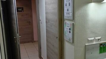 Ein Flur mit einer Tür, auf der „103“ steht, die zu einem Raum führt. An der Wand befinden sich Schilder, die ein Restaurant namens „L PARCO“ mit einer Speisekarte und einem QR-Code bewerben.