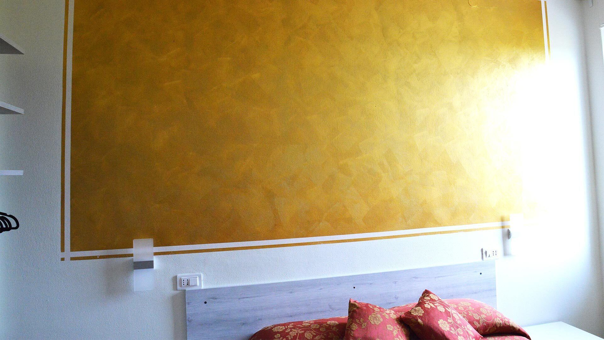A room with a bed, a headboard, and a large yellow wall.