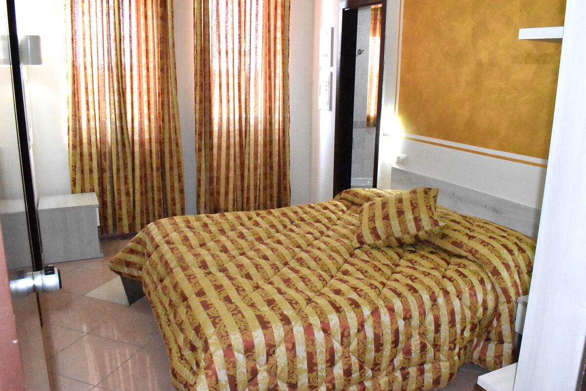 Une chambre d’hôtel avec un grand lit, des rideaux, un miroir et un sol carrelé.