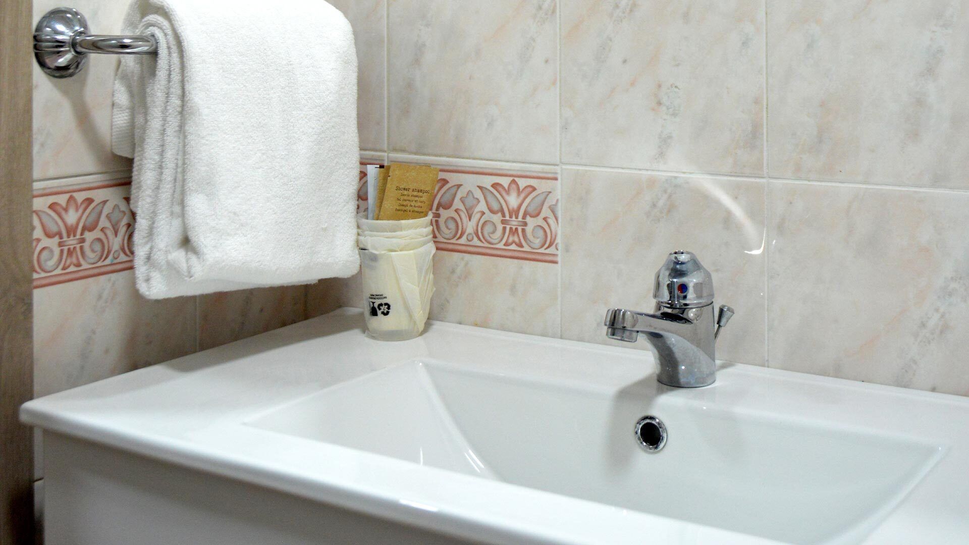 A bathroom with a white sink, a silver faucet, and a towel hanging on a metal towel rack.