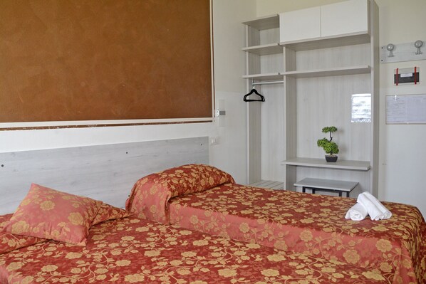 A hotel room with a bed, a small table, a hanging coat rack, and a potted plant.