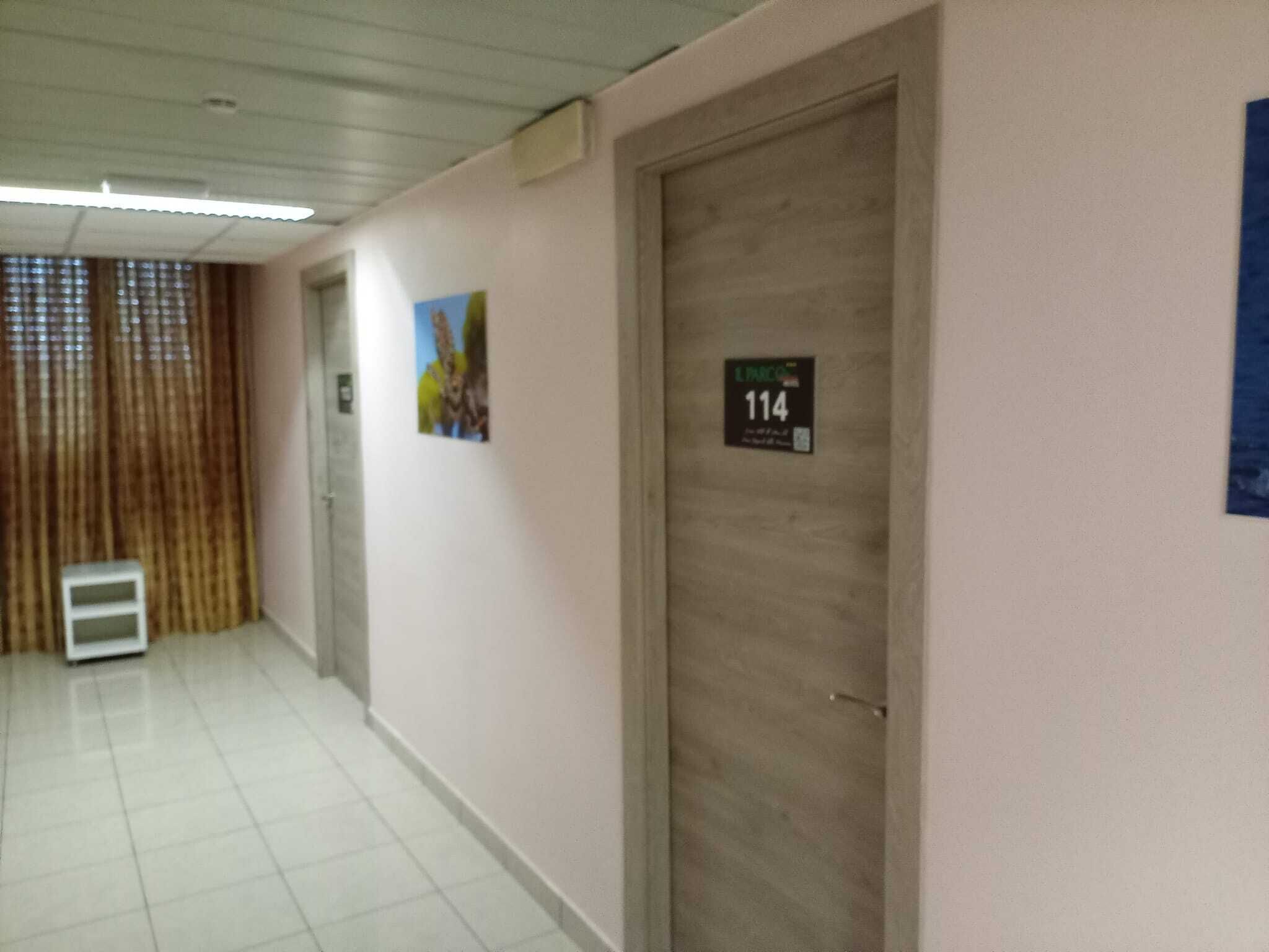 A hallway with a tiled floor, a door labeled '114', and a vent on the wall.