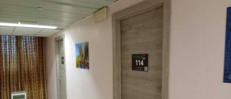 Un passadís amb terra de rajola, una porta amb la inscripció '114' i una reixa a la paret.