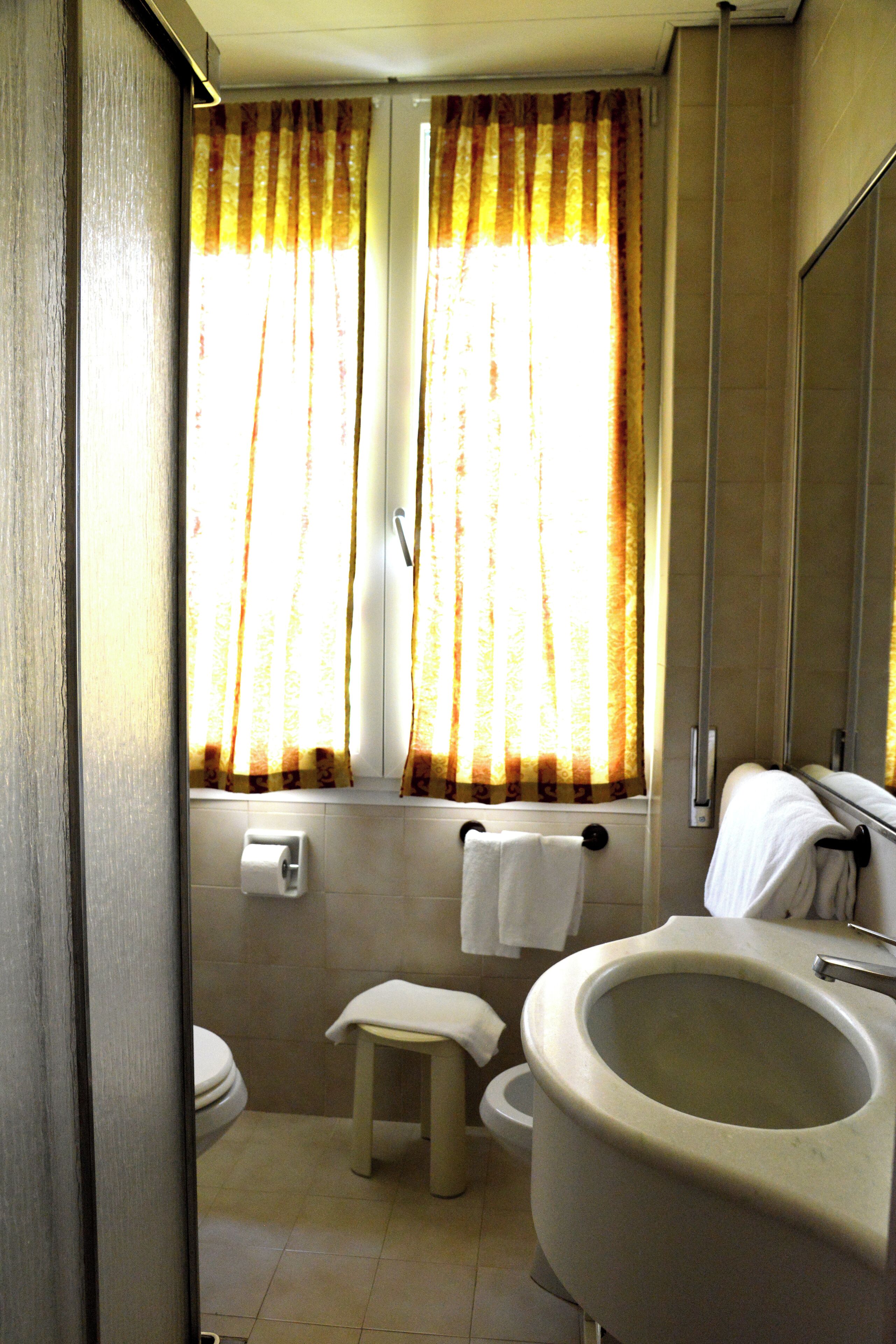 A bathroom with a toilet, sink, and window with curtains.