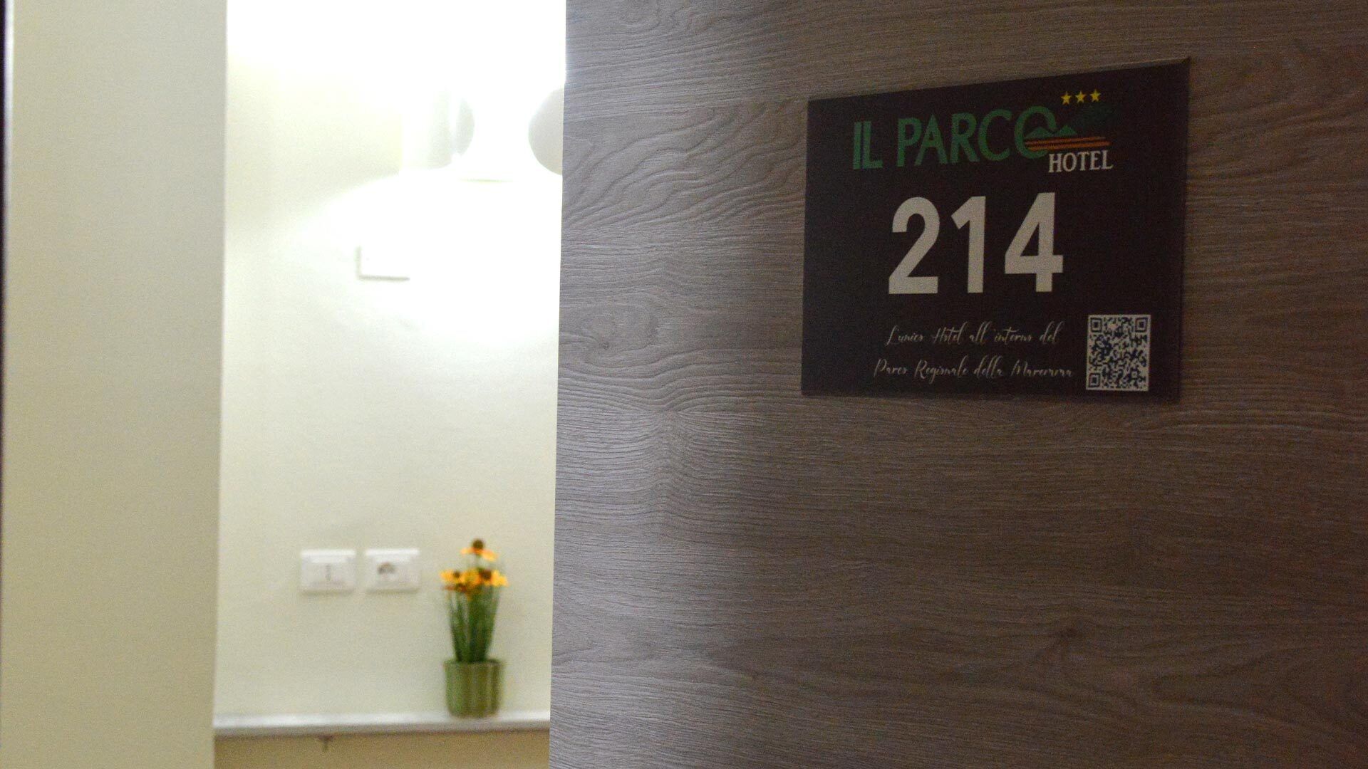 Camera d'albergo con parete in legno, cartello con il numero '214' e un codice QR.