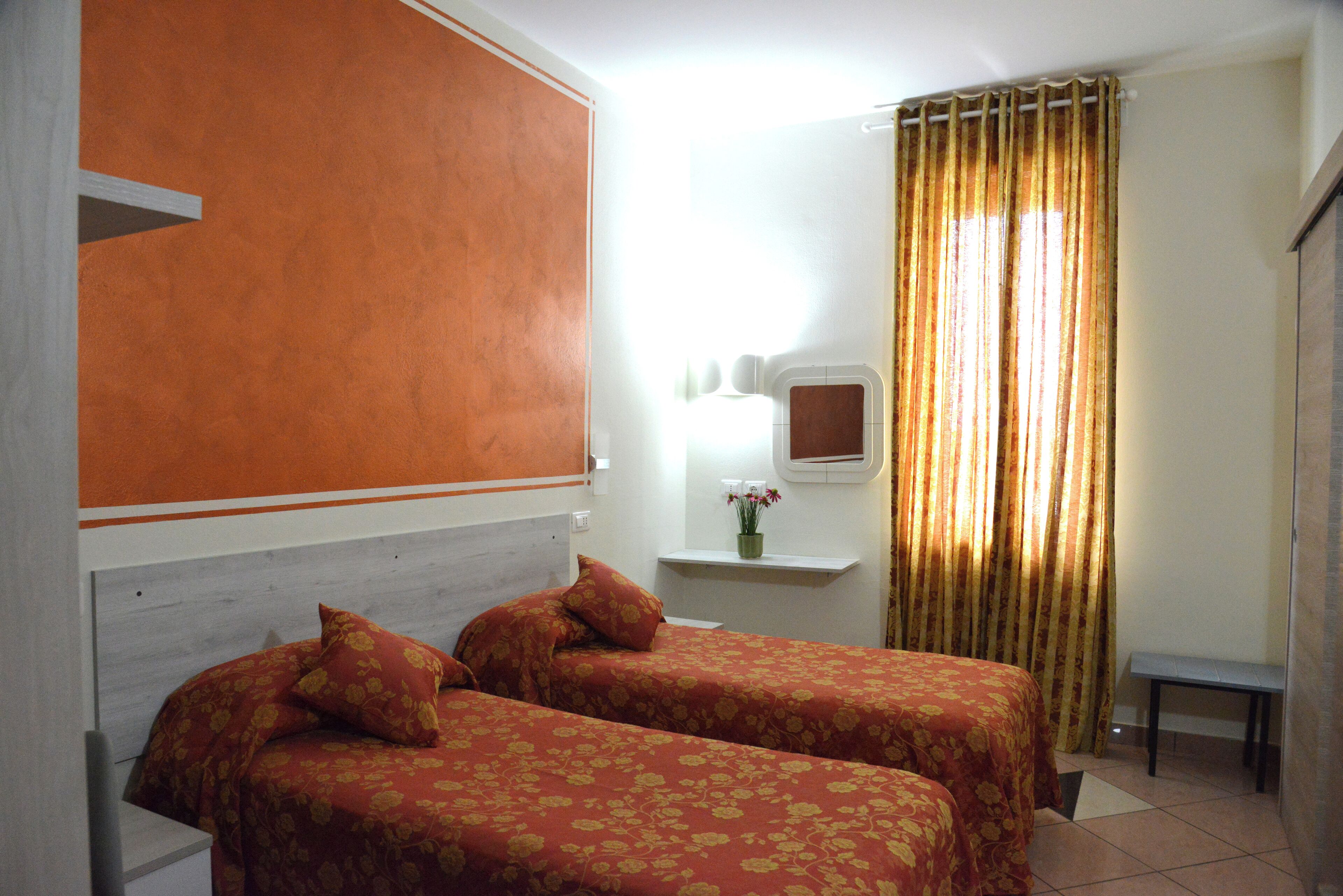 A room with two beds, a small bench, a mirror, and a window with curtains.