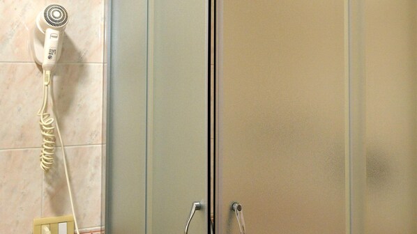 Un baño con un secador de pelo sobre un perchero, una puerta de ducha y un perchero con una toalla.