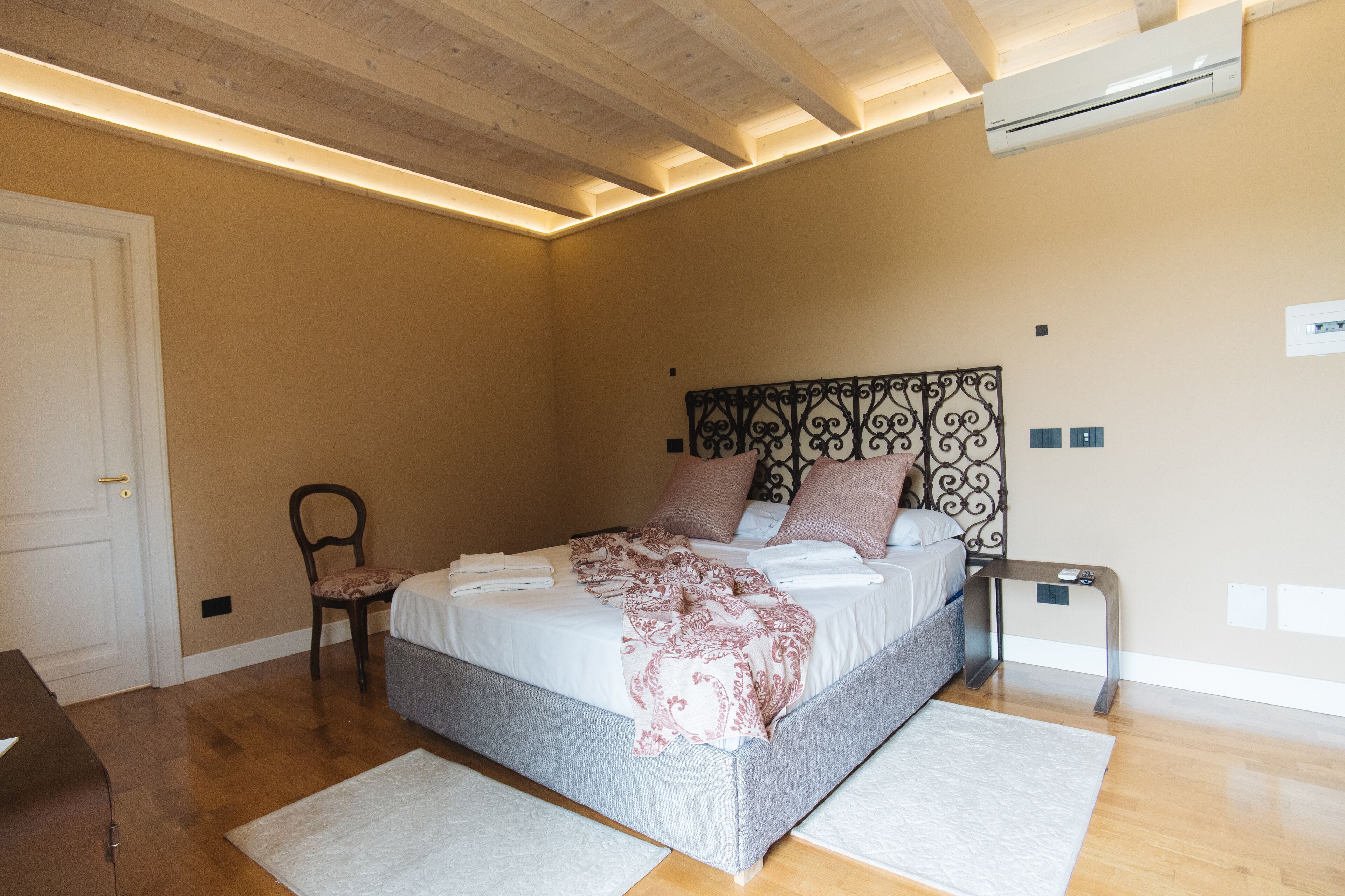 A bedroom with a bed, a chair, a bedside table, and an air conditioning unit.