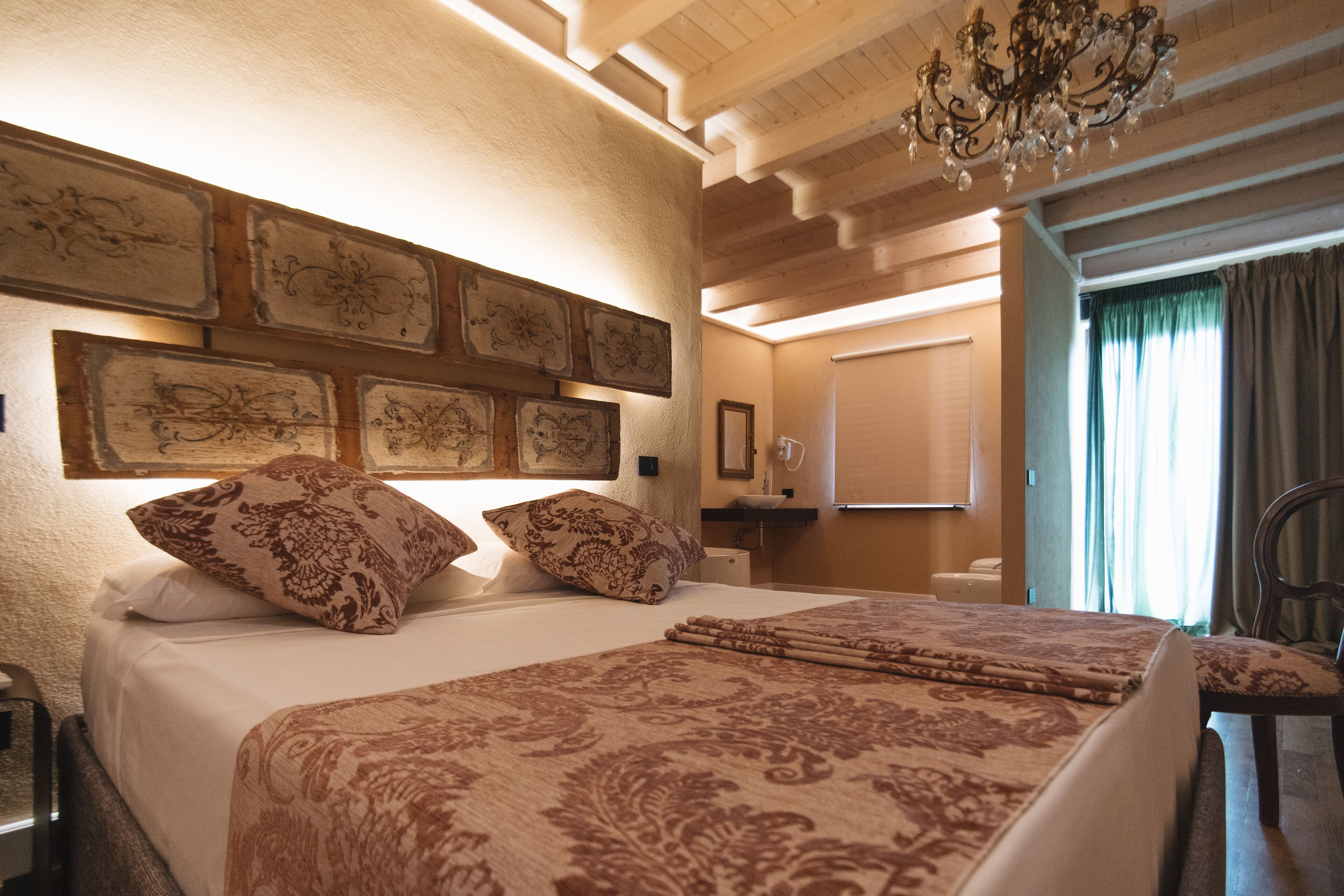 Habitación de hotel con una cama grande, varios almohadones, una araña y vistas al exterior a través de una ventana.